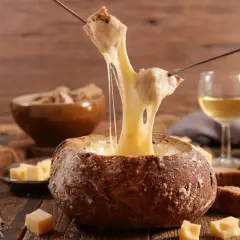 Un pain creusé sert de bol pour une fondue au vin blanc dégoulinante. Des morceaux de pain et de fromage sont prêts à être trempés.