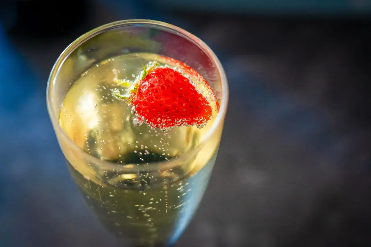 Une fraise flotte dans un verre de soupe angevine pétillante, créant une image rafraîchissante.