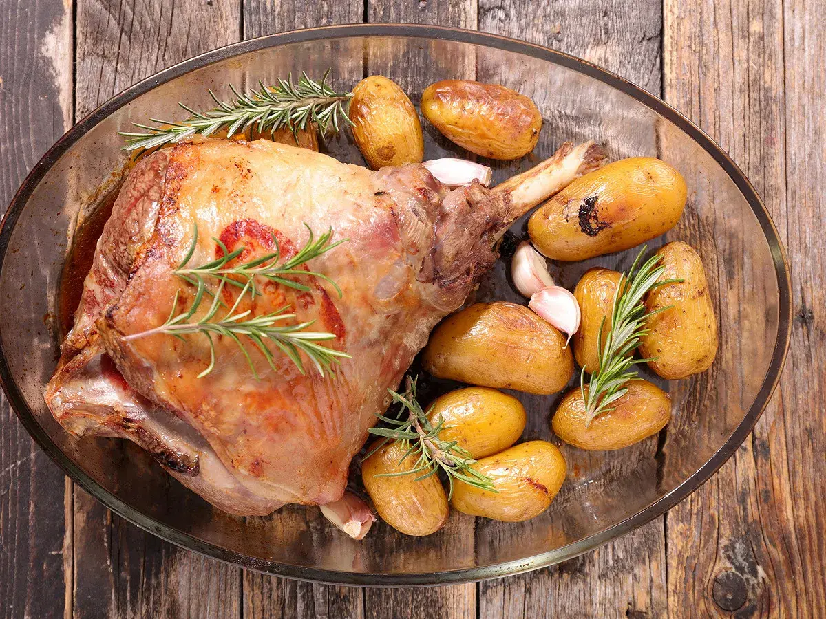 Gigot d'agneau rôti, doré et savoureux, accompagné de pommes de terre grenaille et d'ail, prêt pour la cuisson.