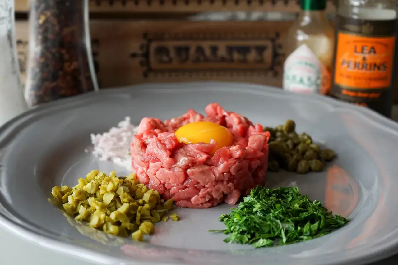 Un plat de tartare de boeuf frais, garni d'un jaune d'oeuf, avec des câpres, des cornichons hachés, des échalotes et du persil.