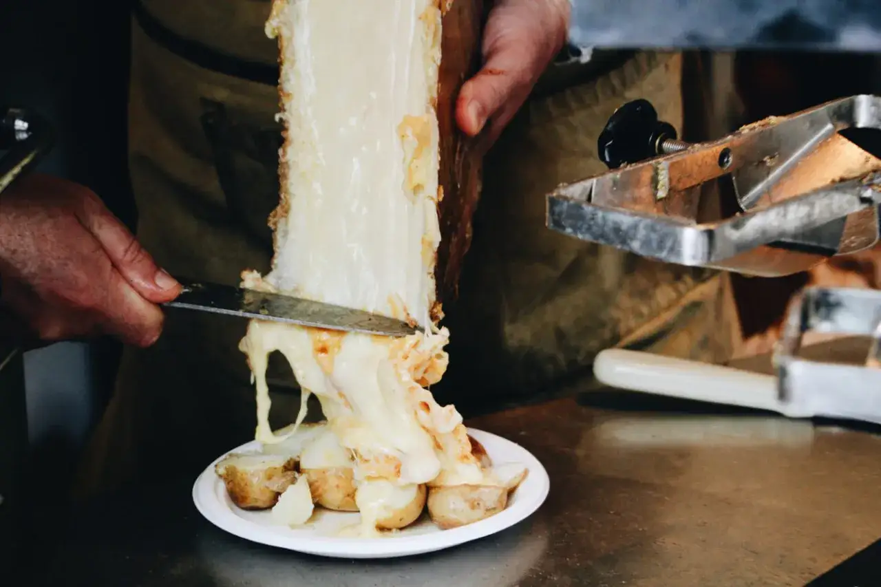 Un couteau gratte un fromage fondant pour le racler sur des pommes de terre. Le fromage dégouline, promettant un délice de raclette.